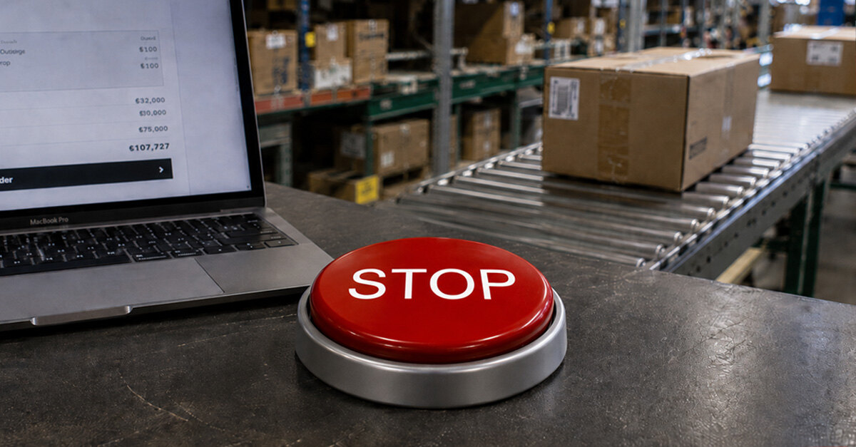 Een rode stopknop naast een laptop, met op de achtergrond een transportband in een magazijn.